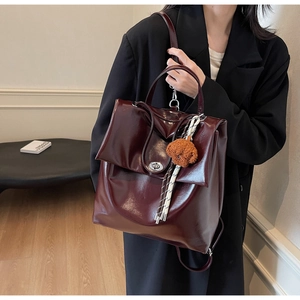 Detail of dark burgundy glossy leather backpack with plush pendant and metal buckle lock