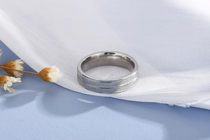 Macro shot of silver brushed stainless steel ring with center groove on white satin