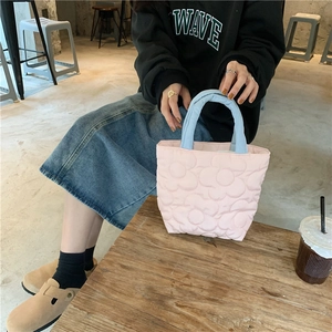 Close-up of pink quilted mini tote bag with flower pattern and blue handles in cafe