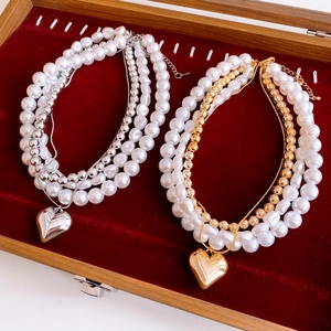 Detail of layered gold and silver heart necklaces with baroque pearls on red velvet