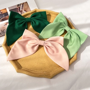 Close-up of three satin bow hair clips in green and pink on a ceramic tray