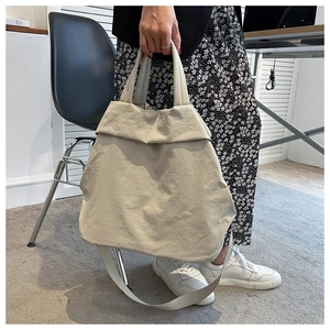 Close-up of lightweight beige nylon tote bag being held by a model in a minimalist setting