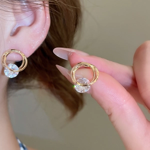 Close-up of golden intertwined circular stud earrings with a large brilliant round zircon