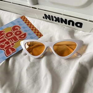 Detailed view of white cat-eye sunglasses with orange lenses on a soft fabric