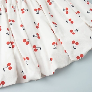Detailed macro view of white crepe fabric featuring a vibrant red cherry print pattern