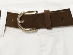 Detail of dark brown frosted belt with gold U-shaped buckle on white high waist jeans