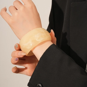 Close-up of marble-textured resin wide bangle in cream yellow on a female wrist