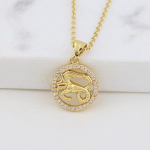 Macro view of gold Capricorn pendant with white stones on a marble surface