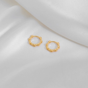 Macro shot of gold-plated bamboo texture hoop earrings on white silk background