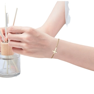 Minimalist gold stainless steel cross bracelet for women worn on wrist in a lifestyle setting