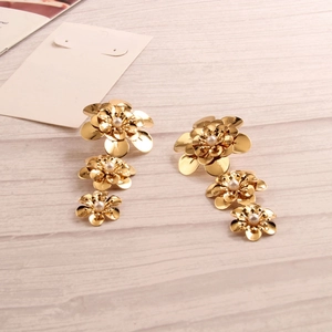 Close-up of golden triple-layered flower drop earrings with white pearl centers