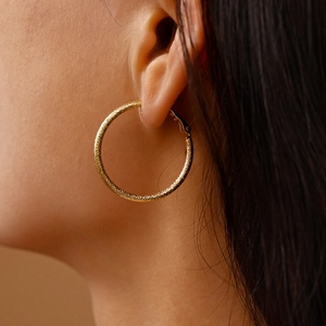 Close-up of a large gold hoop earring with a textured glitter finish on a model's ear