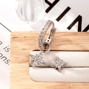 Asymmetric silver star earrings set with sparkling cubic zirconia on a wooden jewelry tray