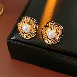 Detailed shot of vintage gold flower earrings with white pearl on black leather texture