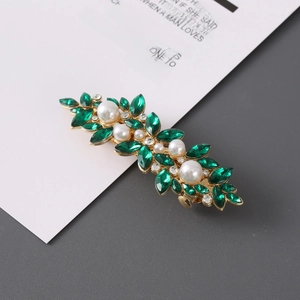 Detail of leaf-shaped gold hair clip with green rhinestones and white pearls on card