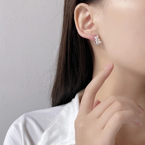 Close-up of a silver cute bear stud earring worn by a model in soft lighting