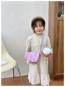 Girl wearing a purple round crossbody bag with shiny pink wings in a cozy indoor setting