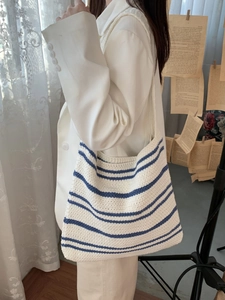 Detail of hand-woven white tote bag with blue stripes worn by a model in soft lighting