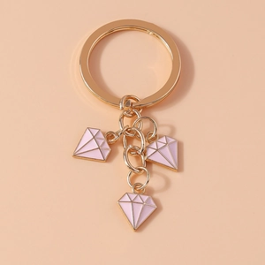 Close-up of golden alloy keychain with three pink enamel diamond charms on a soft pink background