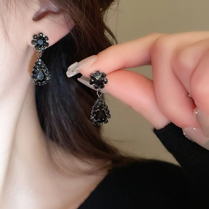 Detail of vintage flower stud earrings with black pear-shaped teardrop pendants on model