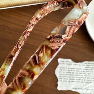 Minimalist U-shaped acetate hair pin with brown marble pattern on wooden surface