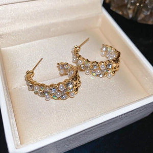 Detailed view of luxury C-shaped gold hoop earrings with pearls and crystals in a box