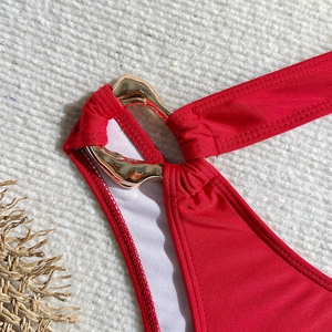 Macro detail of red high-elastic swimsuit fabric featuring a polished gold hardware ring