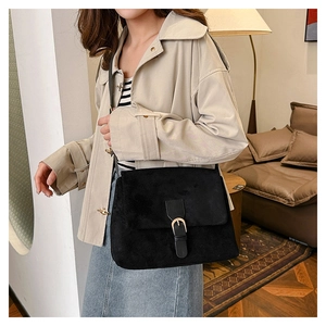 Detail of a vintage black suede crossbody bag with metallic buckle worn by a model