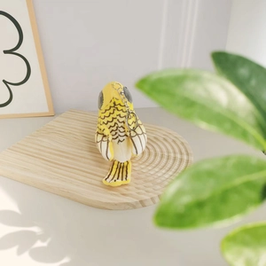 Close-up of a yellow bird plush keychain on a textured wooden surface with soft natural lighting