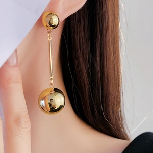 Close-up of a model wearing gold double ball drop earrings with a polished mirror finish