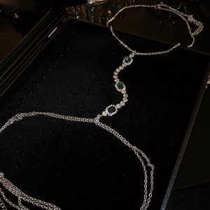 Détail d'une chaîne de corps argentée avec pierres vert émeraude et strass brillants