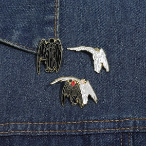 Detail of angel and devil enamel pins on blue denim fabric, black and white metal badges