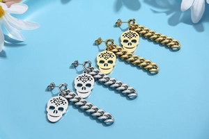 Detail of gold and silver skull earrings with thick Cuban chains on light blue background