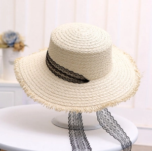 Detail of light beige straw sun hat with black lace ribbon and fringed wide brim