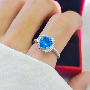 Close-up of a blue gemstone ring with micro-pave diamonds on a model hand with red box