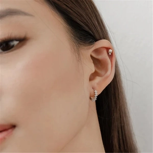 Macro shot of silver crystal hoop earrings and pearl ear cuff on female model