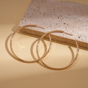 Macro shot of large polished golden geometric hoop earrings leaning against a textured stone