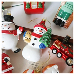 Macro view of Christmas tree ornaments featuring painted snowmen and red locomotives