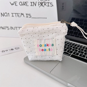 Detail of a small white canvas pouch with black polka dots and sozakka beauté embroidery
