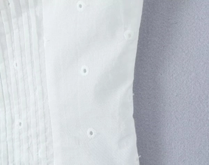 Dettaglio ravvicinato del top in cotone bianco con tessuto a pieghe e ricamo traforato
