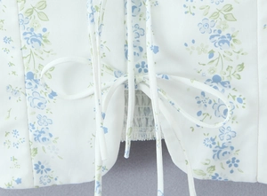 Detailed view of white floral top featuring a blue pattern with tie-up bow and elastic smocking