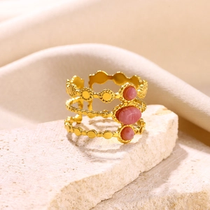 Three-layer gold stainless steel ring with pink stones on a minimalist stone display
