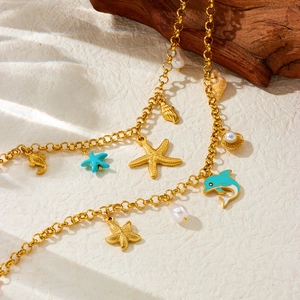 Gold ocean themed necklace with enamel dolphin, starfish and pearl charms on sandy backdrop