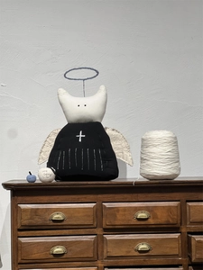 Detail of handcrafted corduroy fabric angel doll with cross embroidery on dark wood dresser