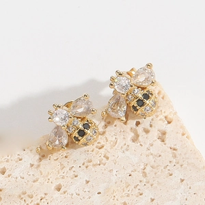 Detailed macro view of bee stud earrings with clear zircons on beige stone