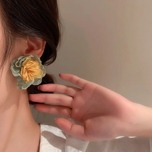 Close-up of large sage green and mustard yellow fabric flower earring on a model