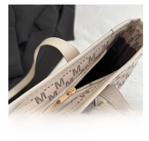Detail view of smooth golden metal zipper on a beige tote bag with M-letter monogram print