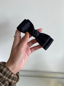 Detail of elegant black satin bow hair clip held to show soft texture and glossy finish
