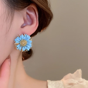 Close-up of blue daisy stud earring with gold center on model's ear for vacation