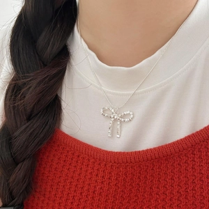 Detail of silver bow pendant necklace worn by model showing minimalist woven metal texture